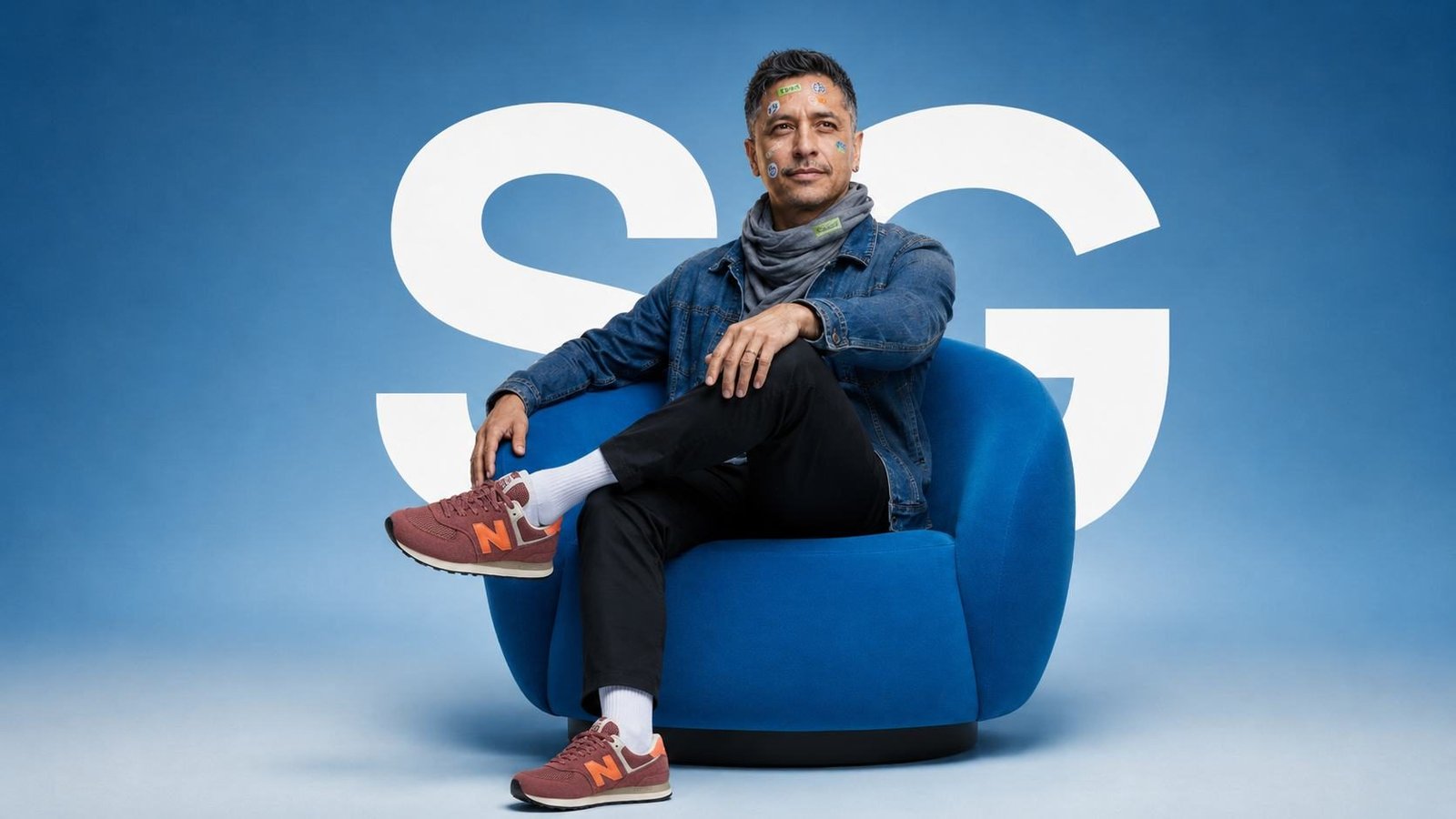 Sandy Galabada seated in a blue chair in front of an oversized SG monogram.